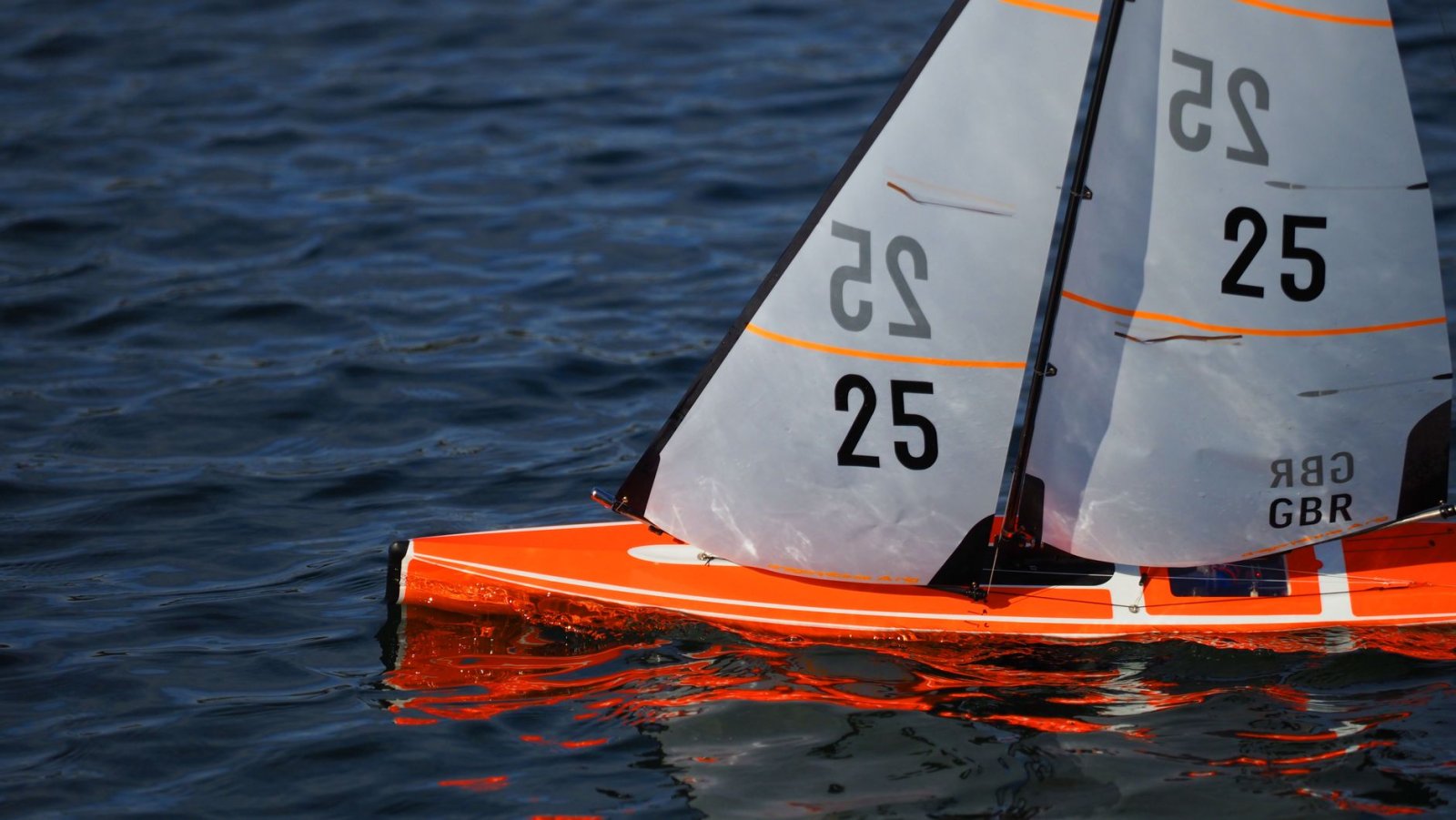 Close-up of an orange model sailboat reflecting on lake waters in Pontefract, England.
