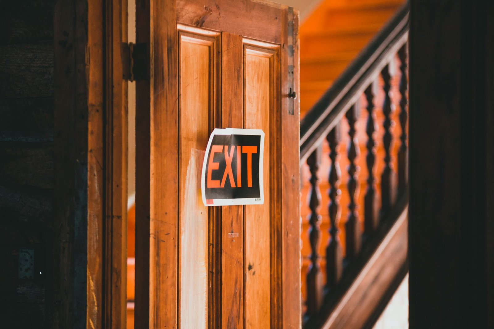 Wooden door with a red exit sign in a rustic indoor setting with staircase.