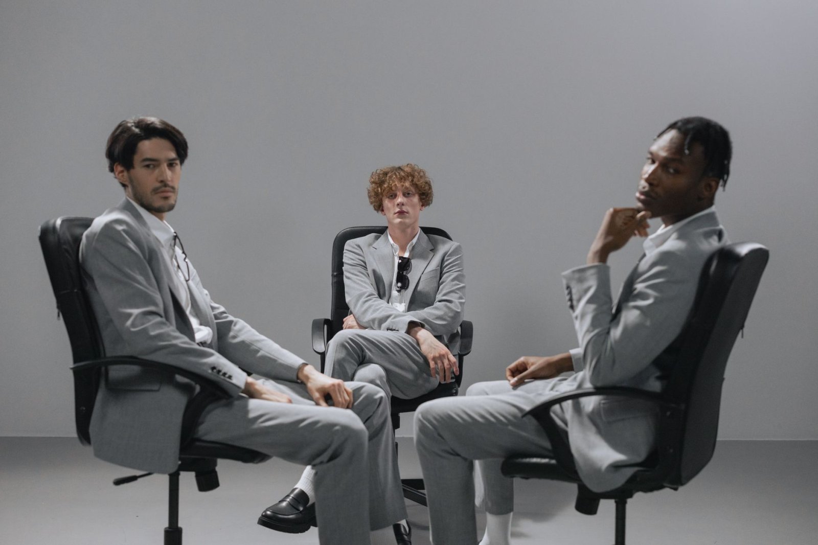 Three businessmen in grey suits sit in office chairs, conveying a serious work environment.