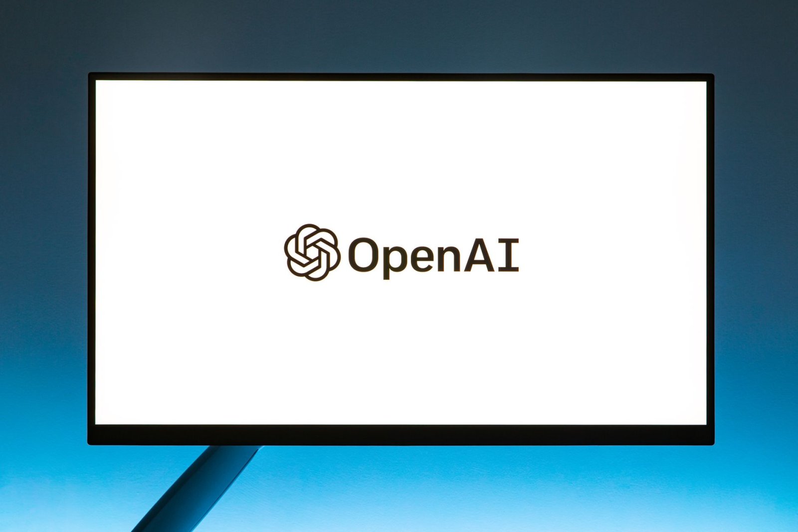 Minimalistic display of OpenAI logo on a monitor with a gradient blue background, representing modern technology.