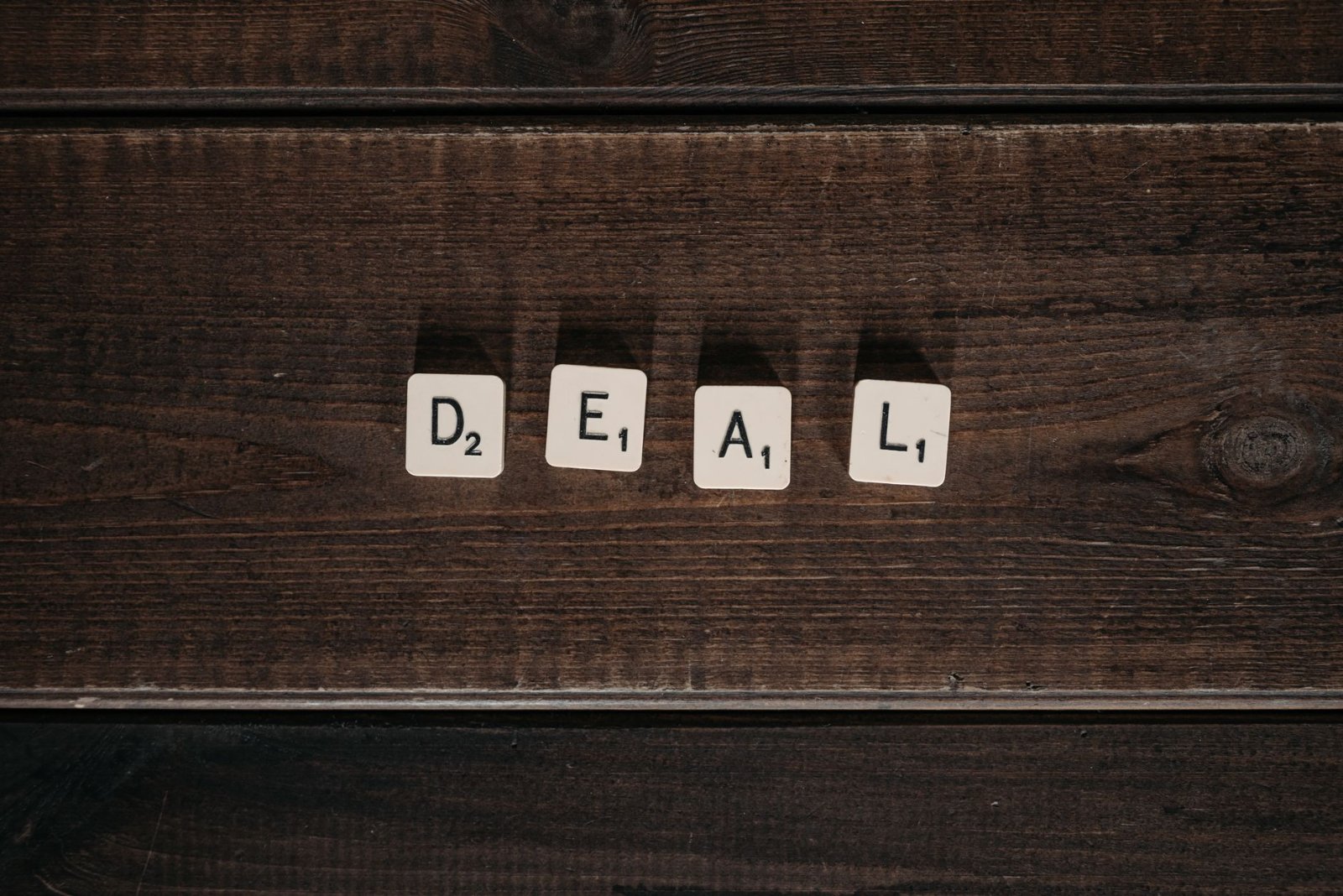 Scrabble tiles spelling 'DEAL' on a rustic wooden surface, viewed from above.