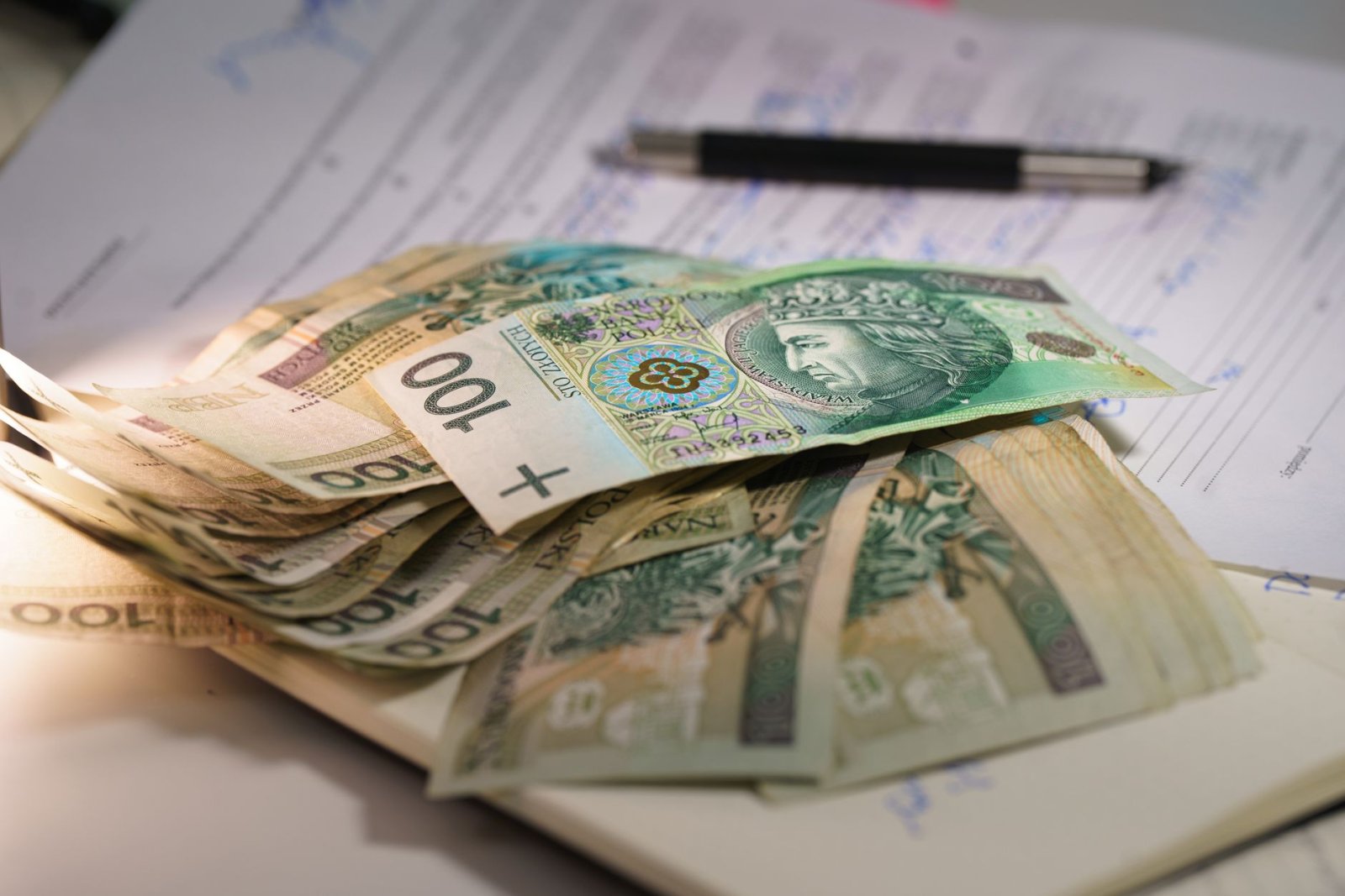 Stack of Polish zloty banknotes on financial documents with a pen, indicating monetary transactions in an office setting