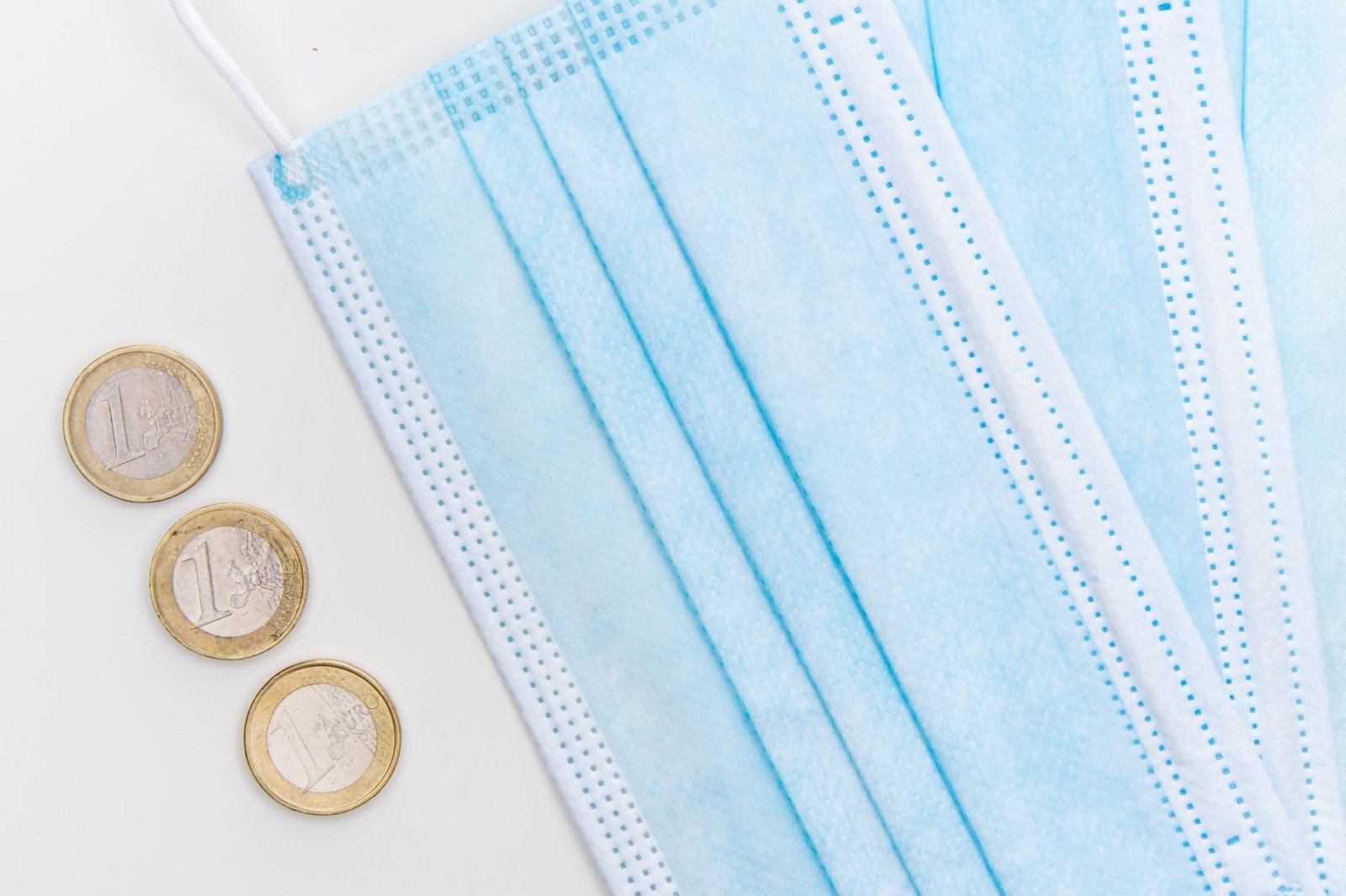 Flatlay of surgical face masks and euro coins, symbolizing pandemic economic challenges.