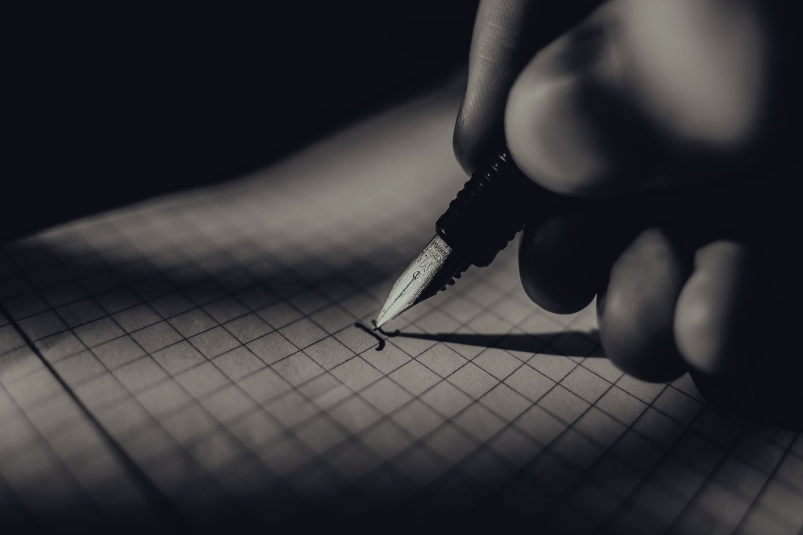 Artistic black and white close-up of hand writing on grid paper, creating a classic and moody atmosphere.