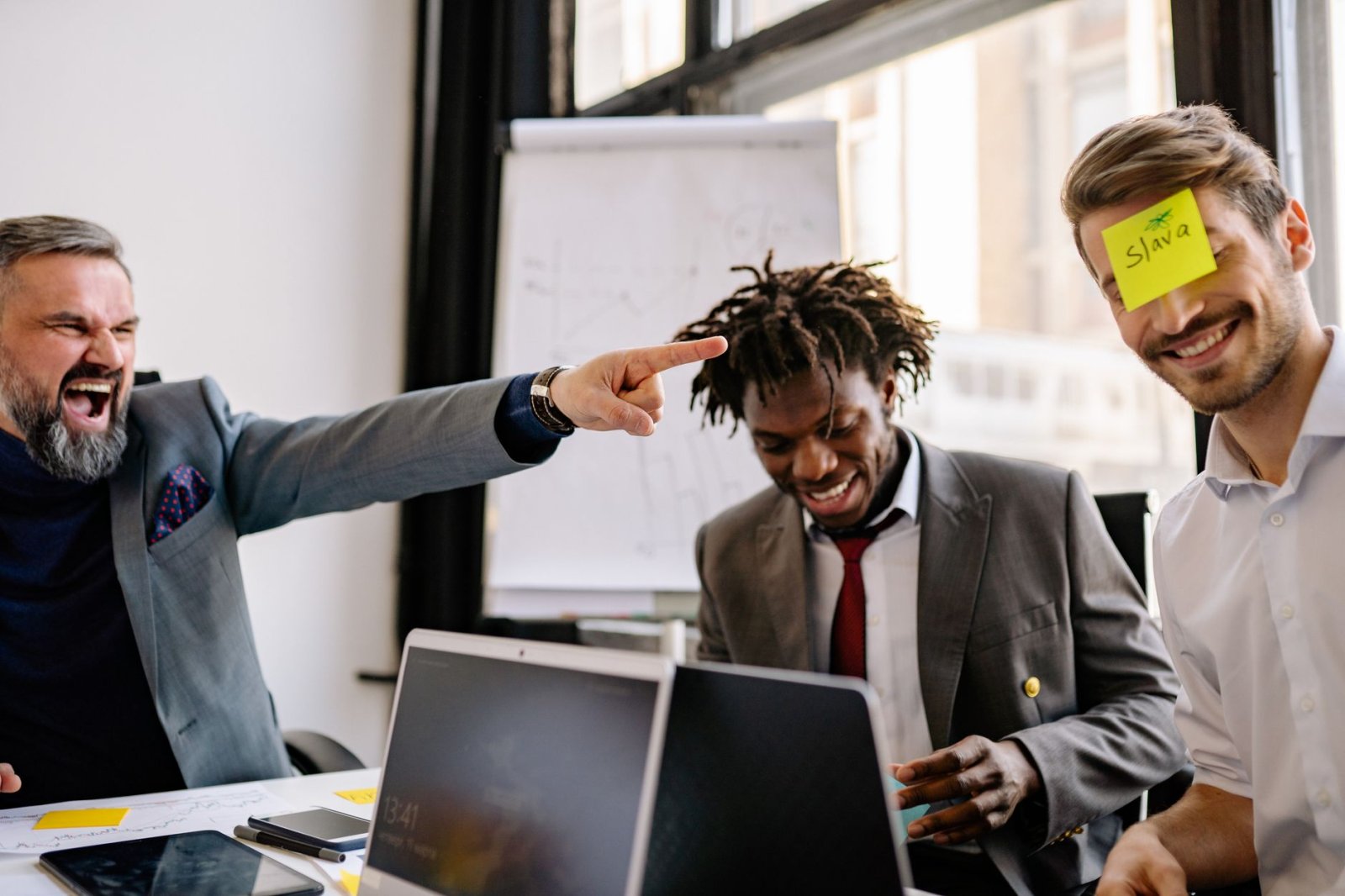 Three diverse colleagues enjoy a lighthearted moment with sticky notes during an office meeting.