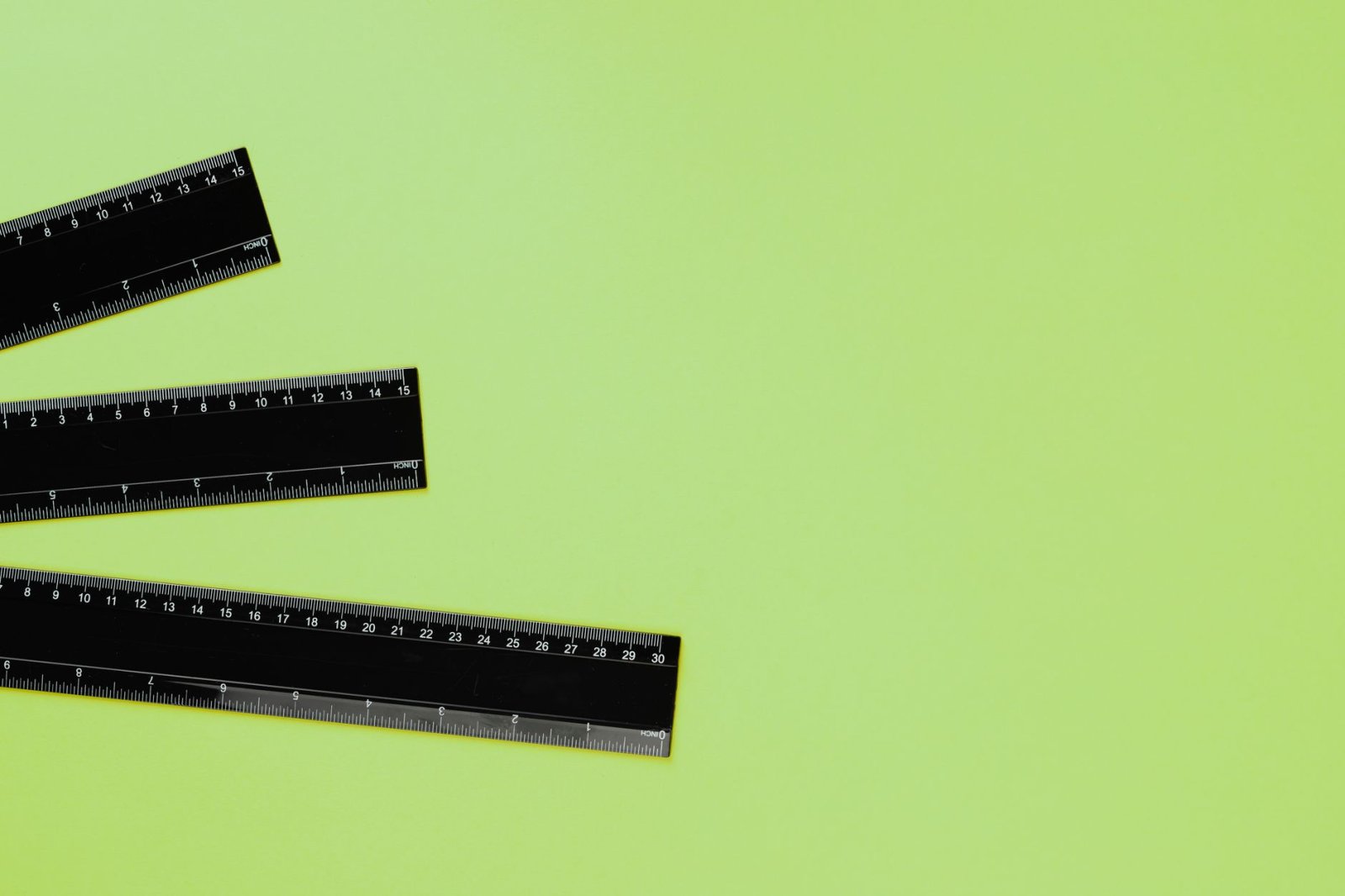 Three black rulers arranged on a vibrant green background, ideal for educational or design contexts.