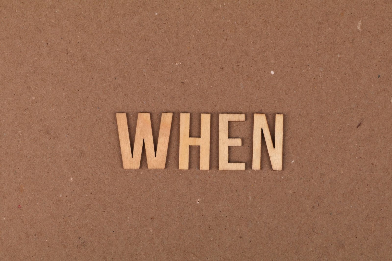 Wooden letters forming the word 'When' on a plain cardboard background.
