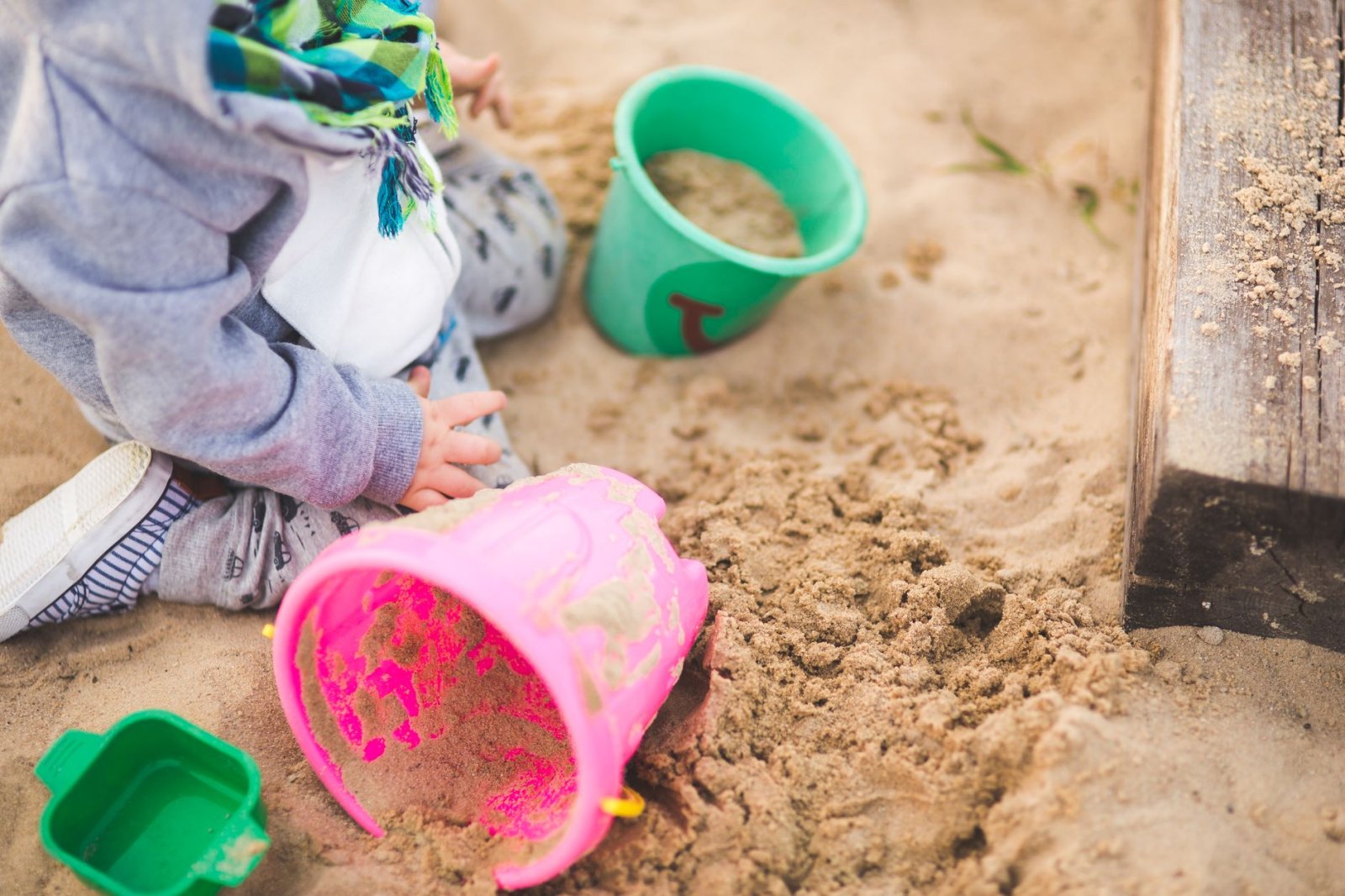 A child enjoys playing in a sandbox using vibrant colored buckets during a sunny day.