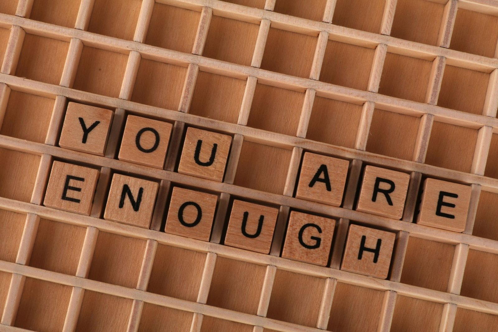 Motivational quote 'You Are Enough' spelled using wooden letter tiles on a wooden grid.