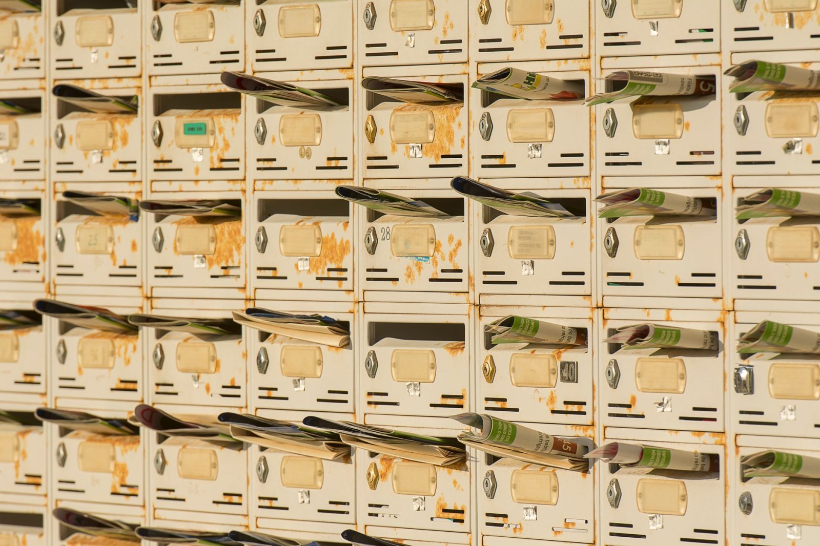 A row of rustic metal mailboxes stuffed with newspapers, creating a vintage urban vibe.