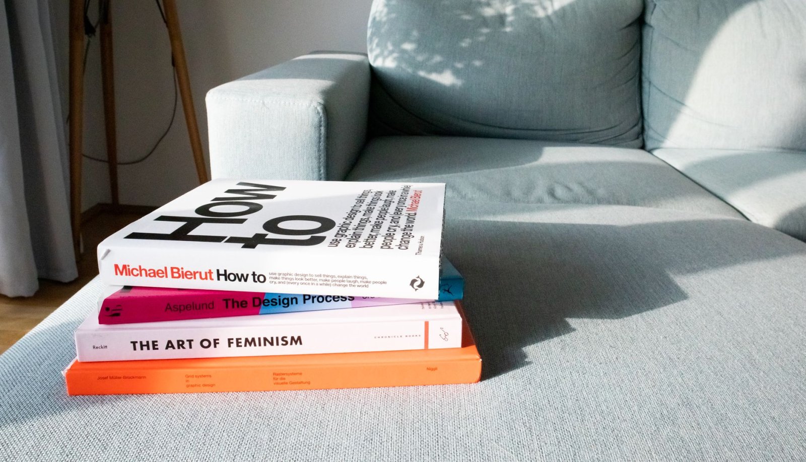 Close-up of design and art books on a modern sofa in a sunlit living room.