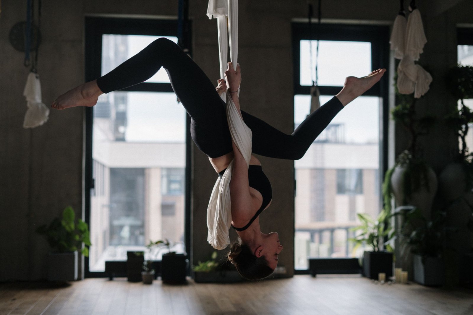 A woman performing aerial yoga in an indoor studio, emphasizing fitness and wellness.
